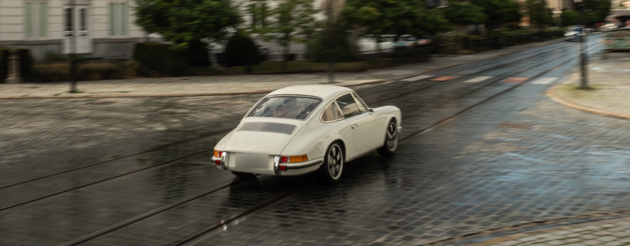 White Revolt Electric driving along a wet street lined with historic buildings